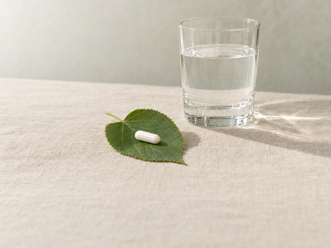 Gélule végétale blanche posée sur une feuille verte, un verre à côté